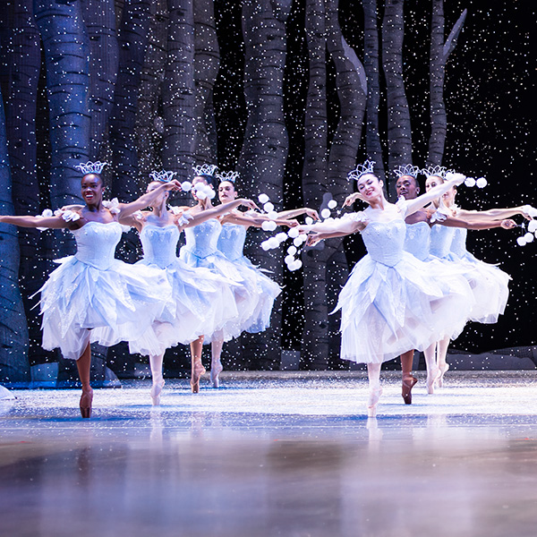 Ballet dancers in white fairy outfits dancing in a forest stage.